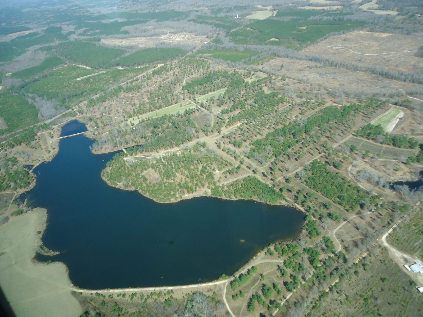 An aerial view shows a lake surrounded by forests and fields, with roads and clearings visible.