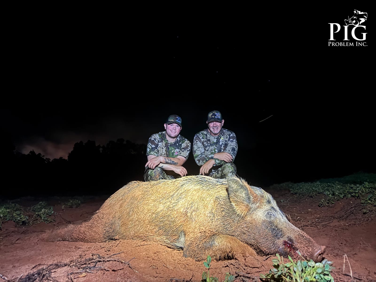 Two hunters pose with a harvested wild boar at night.