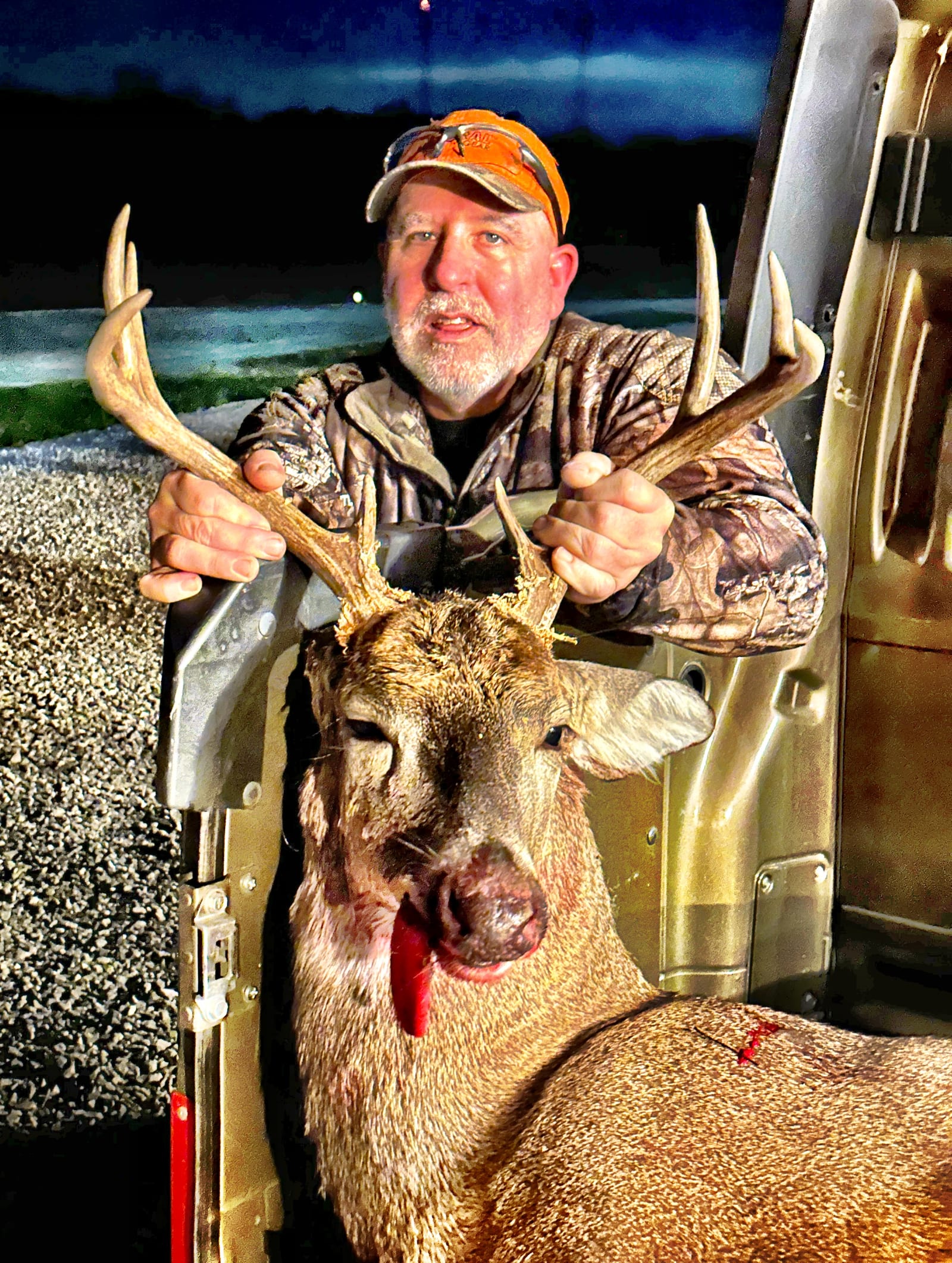 A hunter poses with a harvested whitetail deer at night.