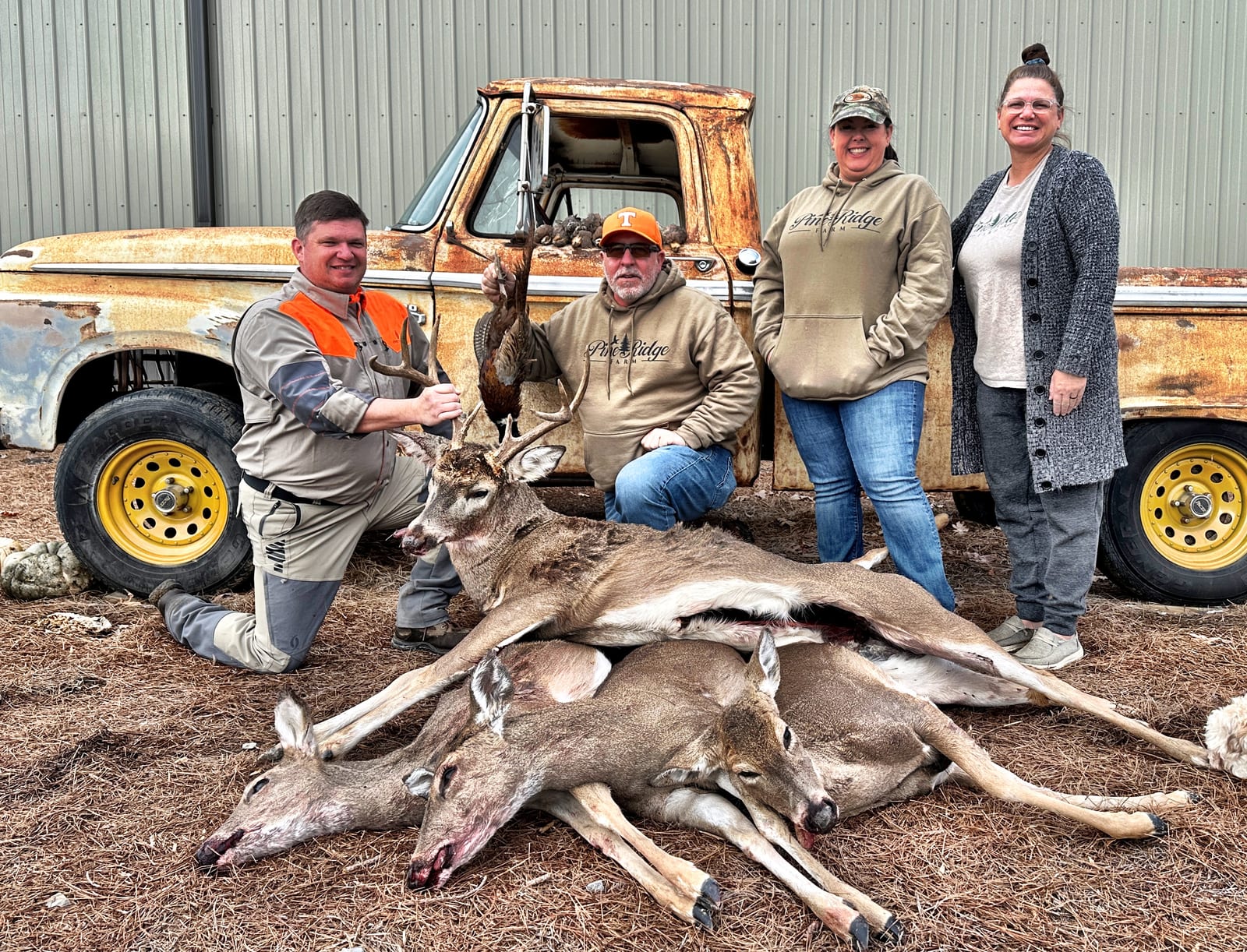 Hunters pose with harvested whitetail deer and a bird in front of an old truck.