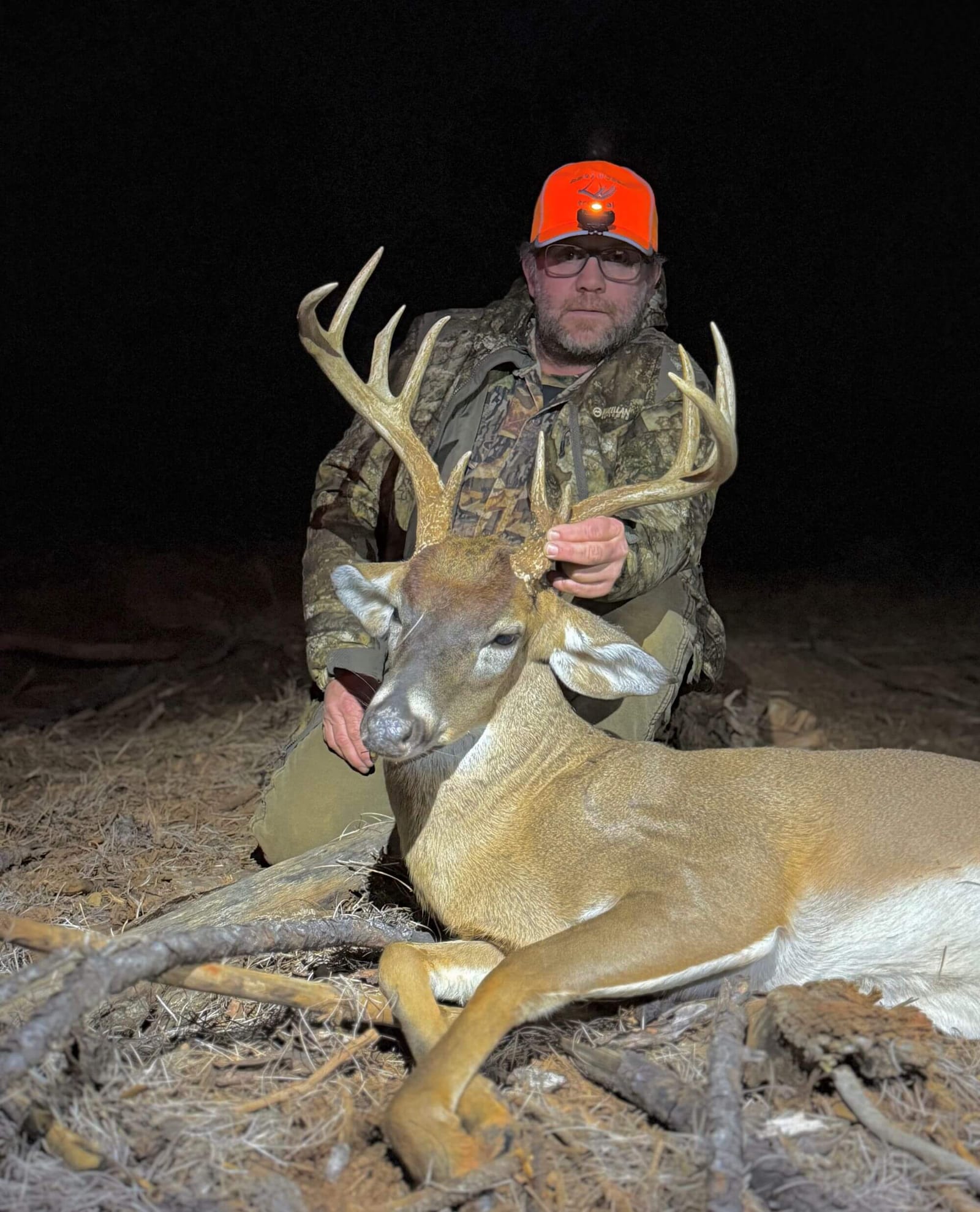 A hunter kneels next to a harvested whitetail deer at night.