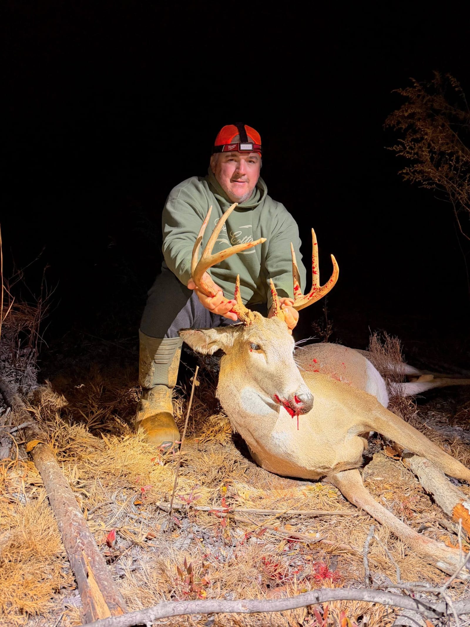 A hunter poses with a harvested whitetail deer at night.