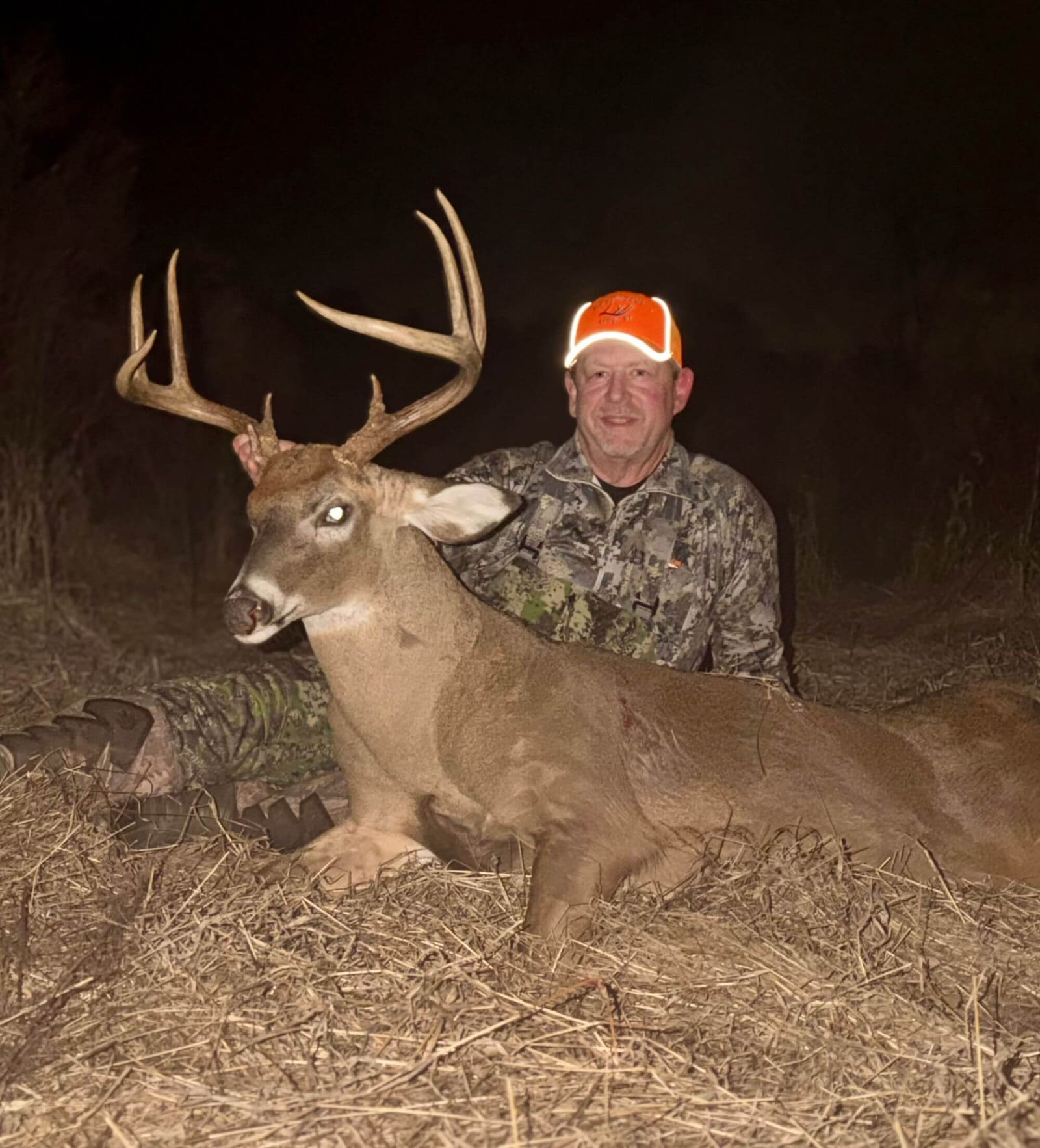 A hunter poses with a harvested whitetail deer at night.