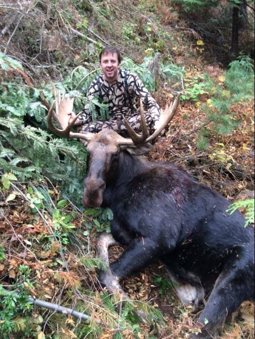A man in camouflage jacket next to a large animal.