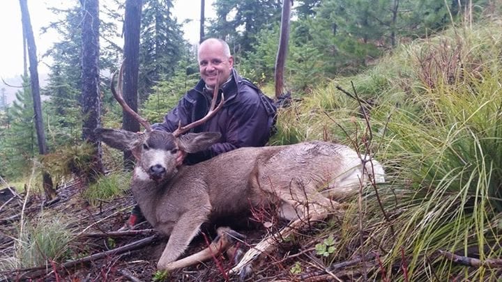 A man kneeling down next to a deer.