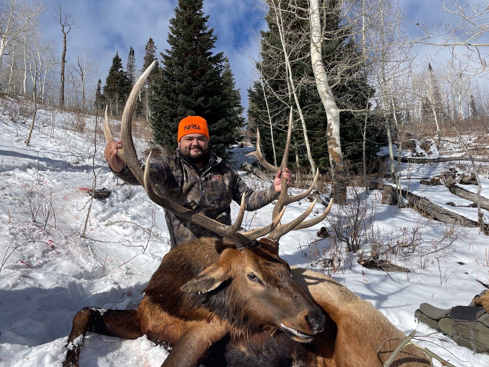 A hunter poses with a harvested elk in a snowy, forested landscape.