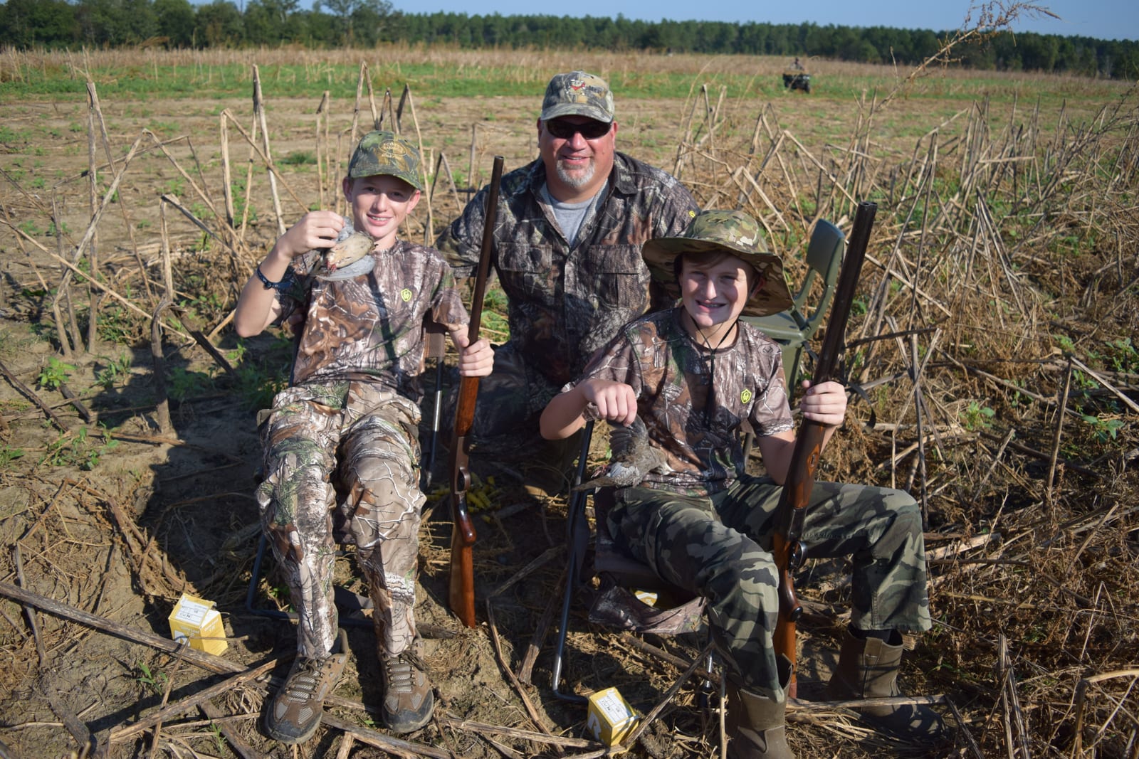 Three hunters, including two boys, pose in a field with a harvested mourning dove.