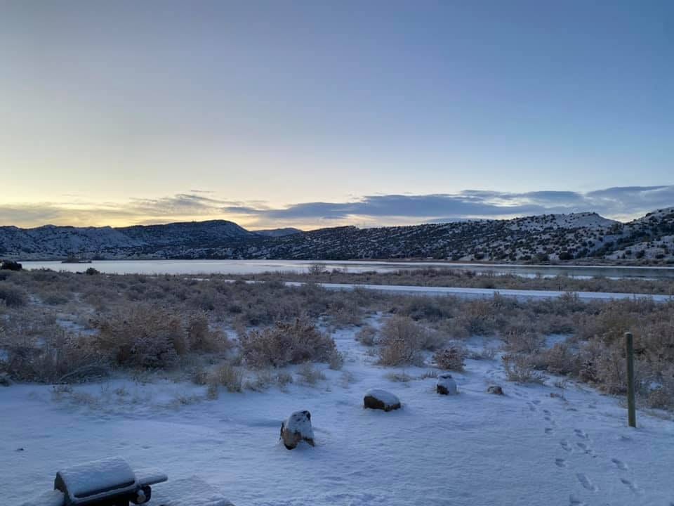 A snowy landscape with a body of water and mountains under a clear sky at dawn or dusk.