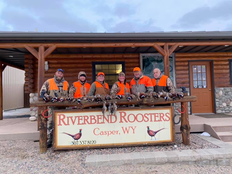 Several hunters pose with harvested ring-necked pheasants in front of a lodge.