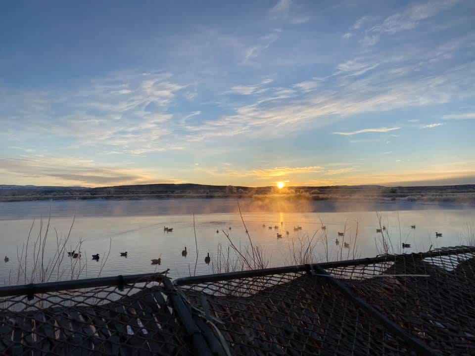 Sunrise over a misty body of water with duck decoys in the foreground.