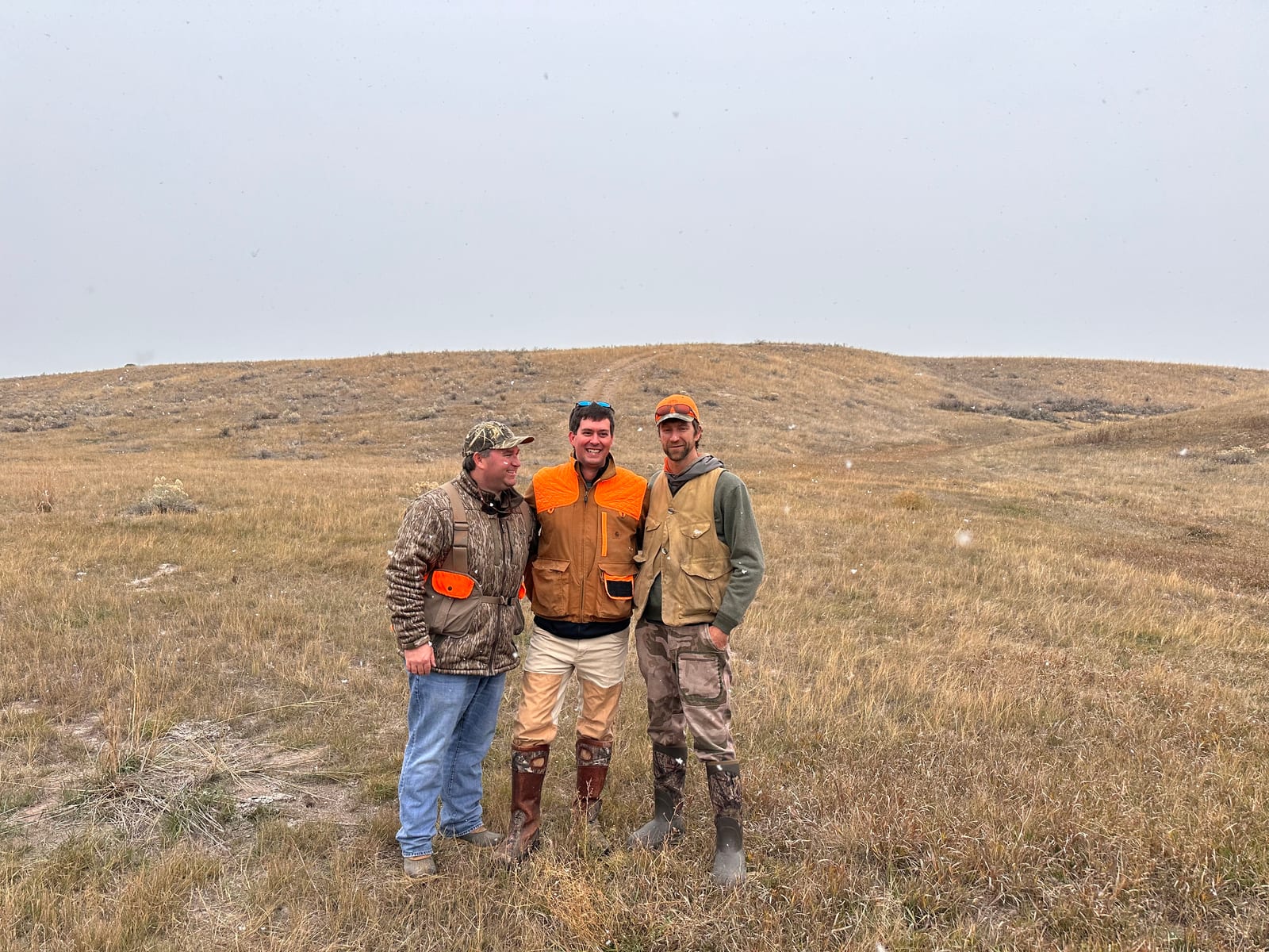 Three hunters stand in a grassy field under a cloudy sky.