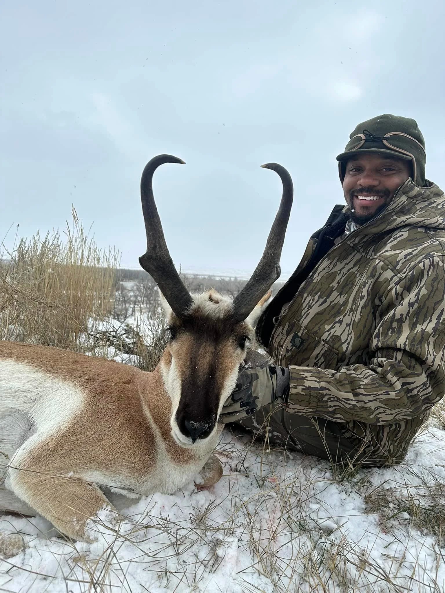 A hunter poses with a harvested pronghorn in a snowy field.