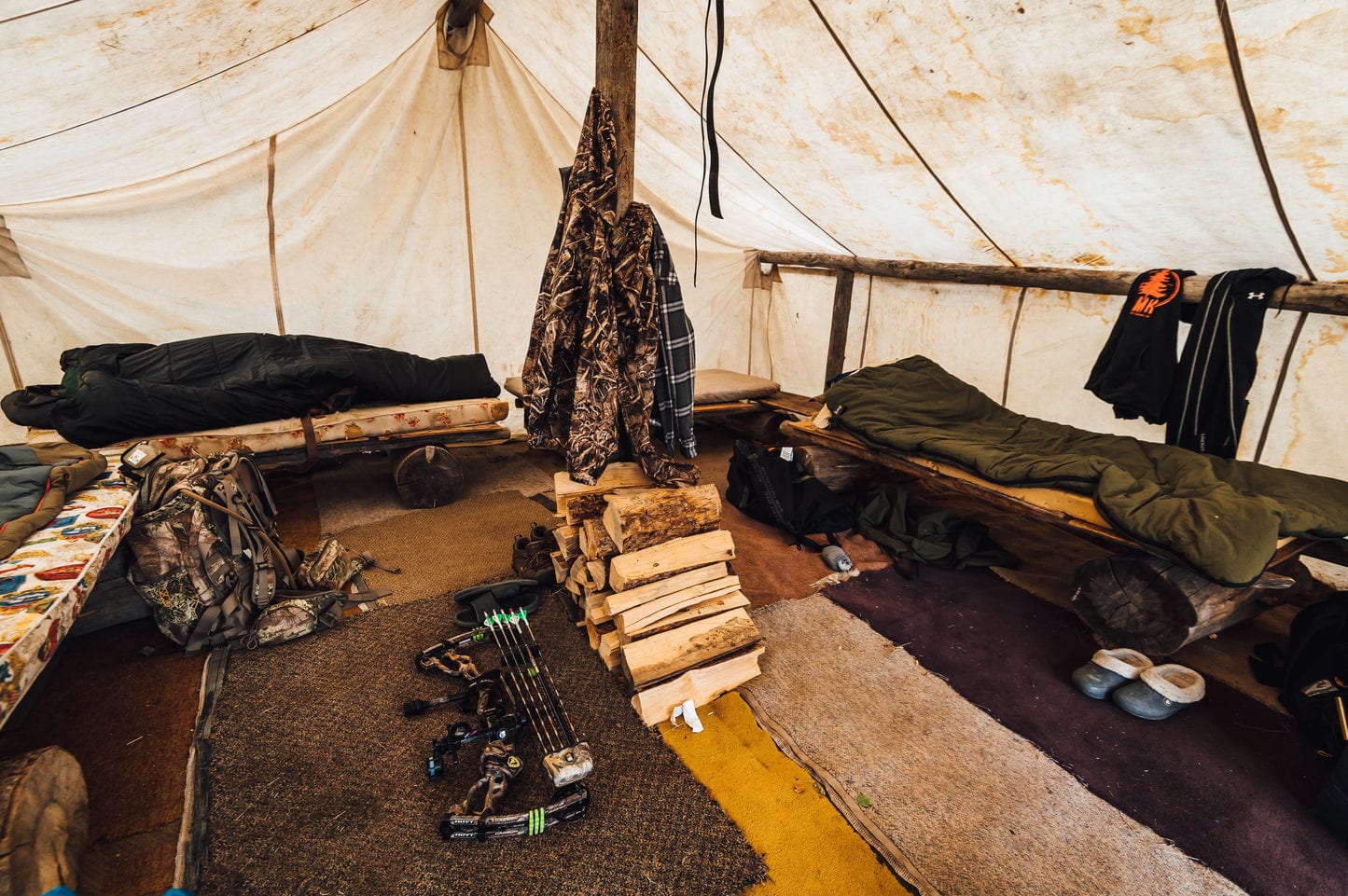 Camping Set Up with cots, sleeping bags, rugs, and fire wood.