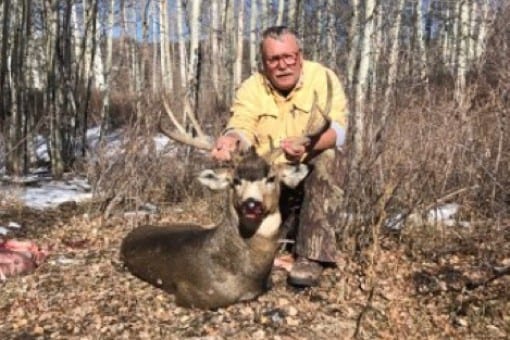 A hunter poses with a harvested mule deer in a wooded area.