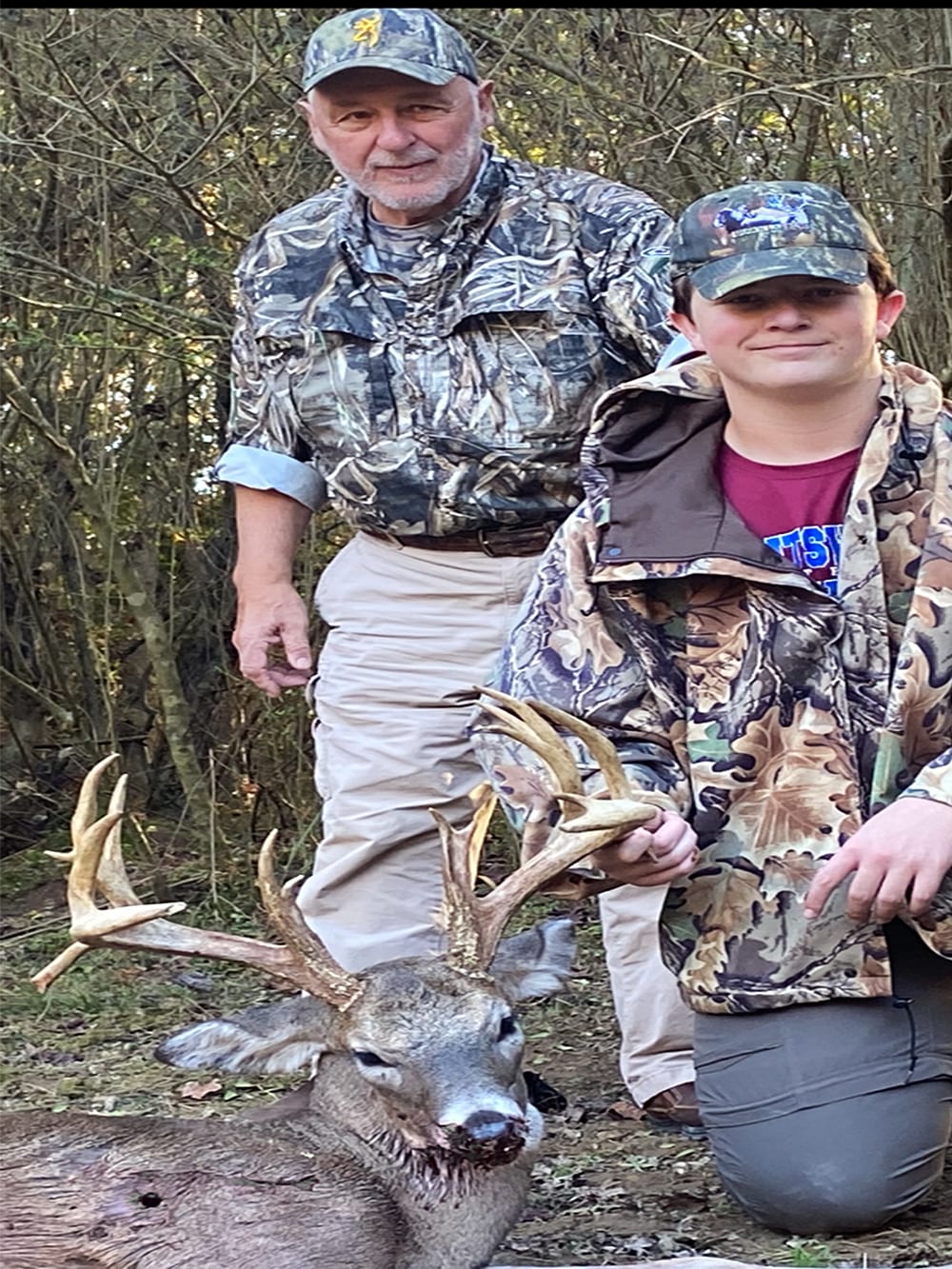 An older man and a younger person pose with a harvested whitetail deer.
