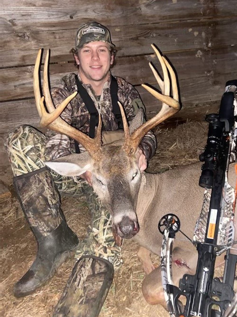 A hunter in camouflage poses with a harvested whitetail deer and a crossbow.