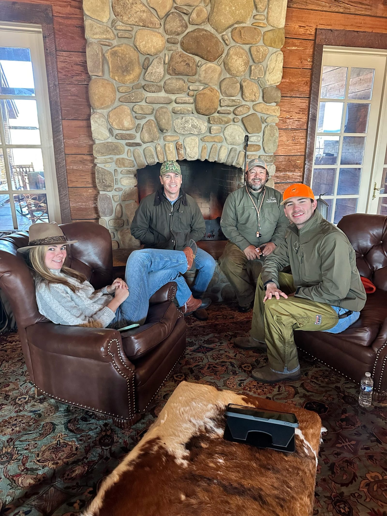 Four people are relaxing in a rustic lodge room with a stone fireplace.