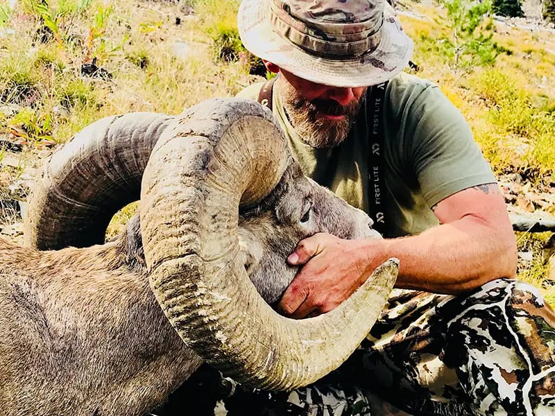 A hunter poses with a harvested bighorn sheep.