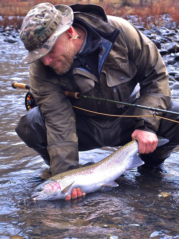 A man in waders and a hat holds a large fish in a river.