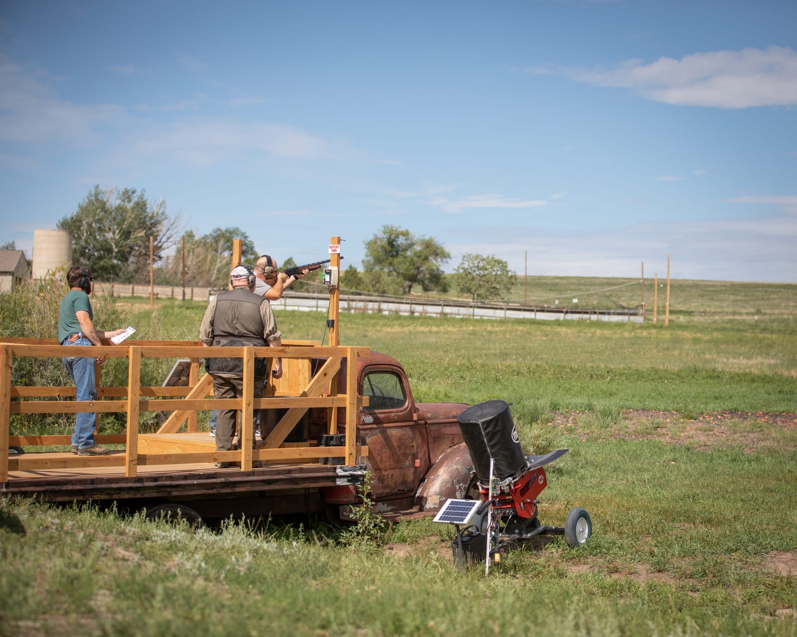 People are shooting clay pigeons from the back of a truck in a grassy field.