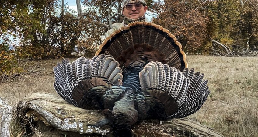 A hunter poses with a harvested wild turkey.