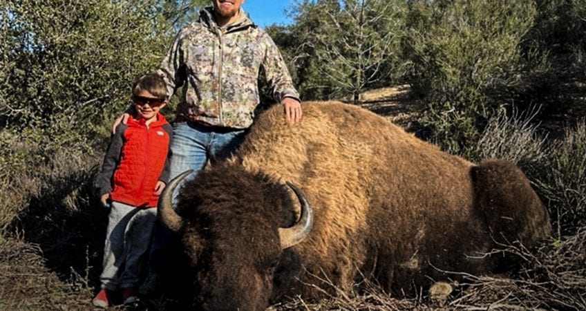A man and a boy pose with a harvested bison.