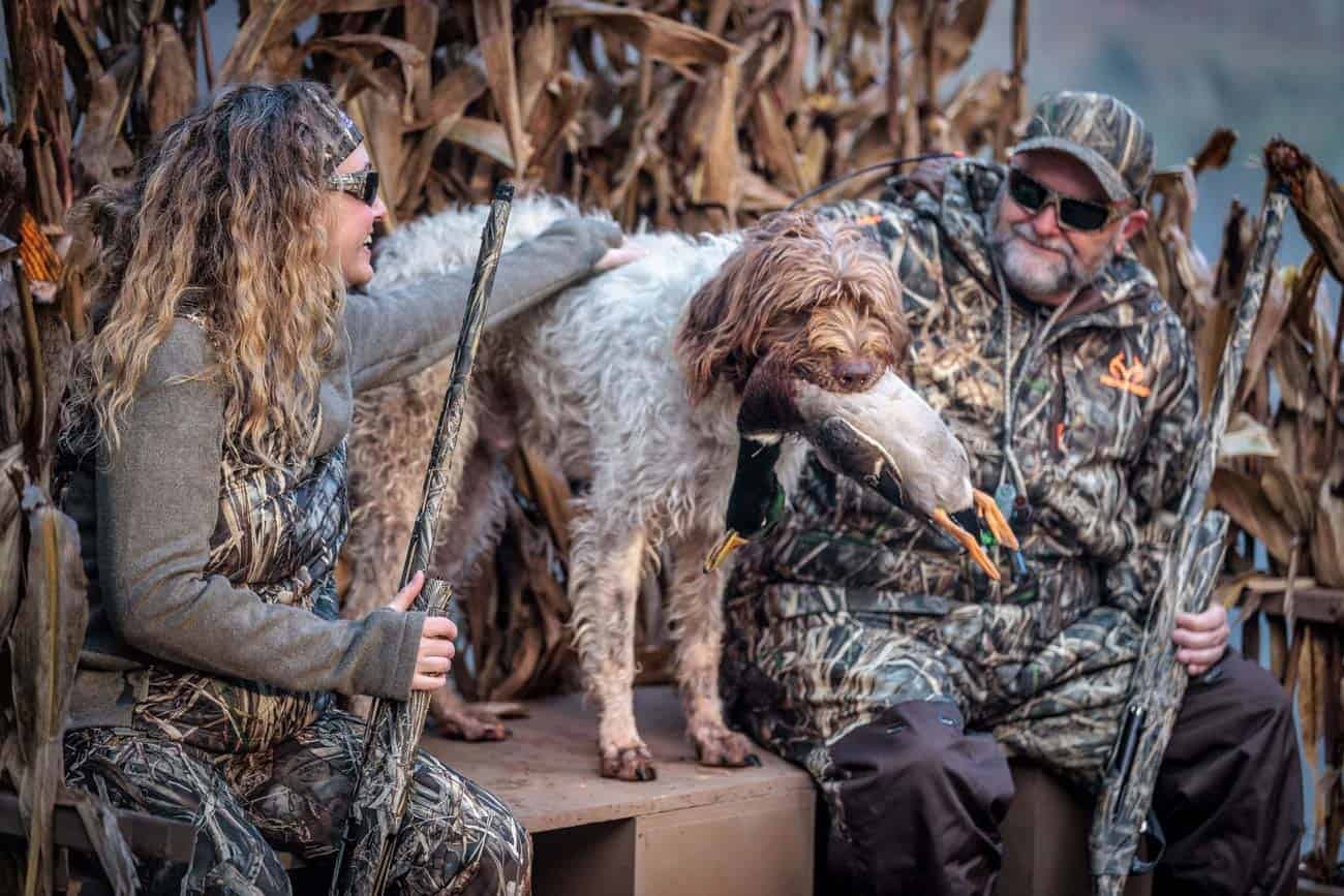 Two hunters and a dog pose with a harvested mallard duck.