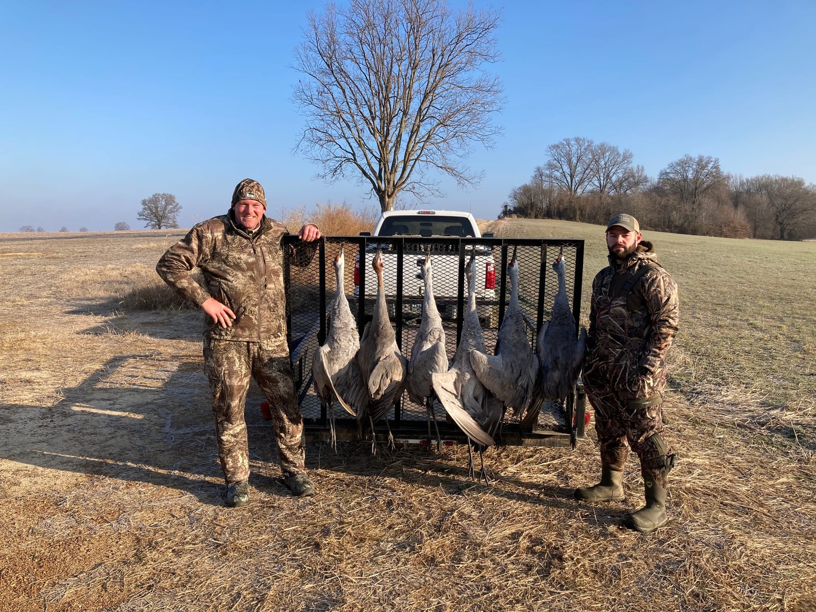 Two hunters pose with their harvested Sandhill Cranes in a field.
