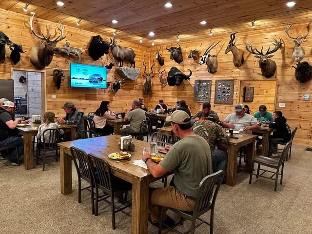 People are dining at tables in a rustic lodge decorated with numerous taxidermy mounts.