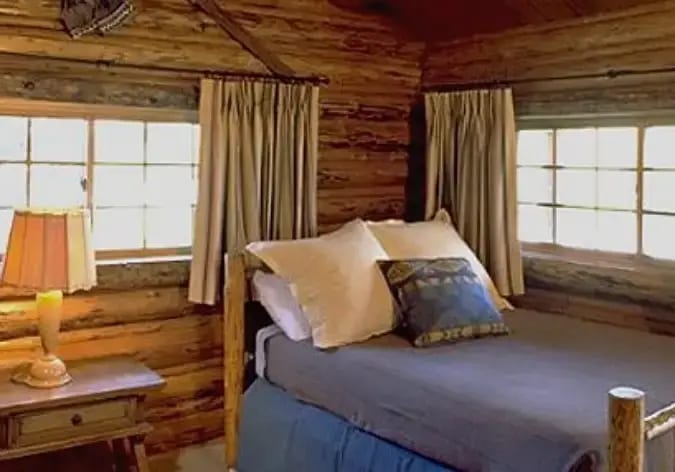 A rustic bedroom with wooden walls, a bed, and a bedside table with a lamp.