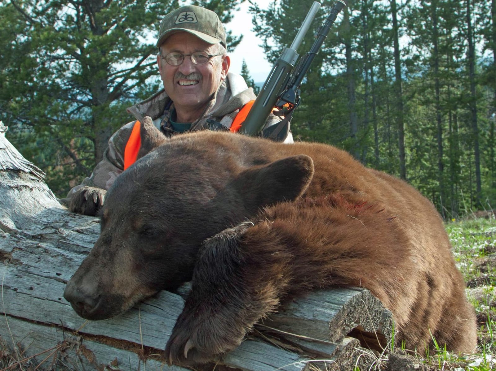 A hunter smiles while posing with a harvested black bear lying on a log.