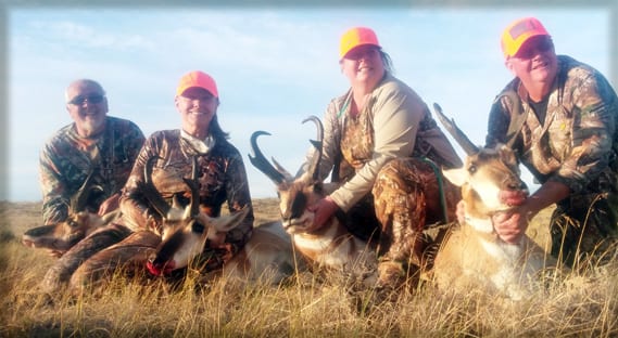 Four hunters pose with their harvested pronghorn in a field.
