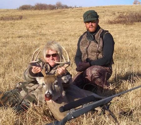 A woman and a man pose with a harvested whitetail deer in a field.