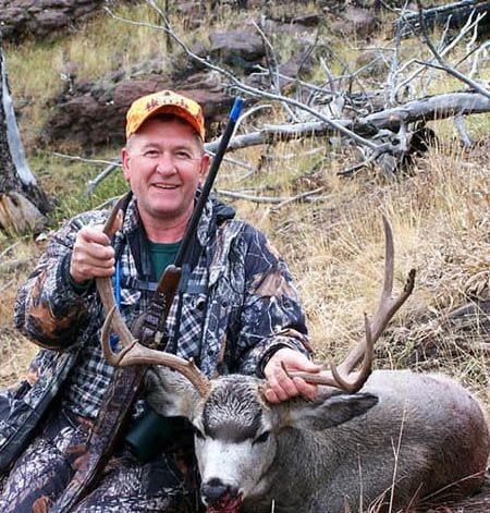 A hunter in camouflage poses with a harvested mule deer.