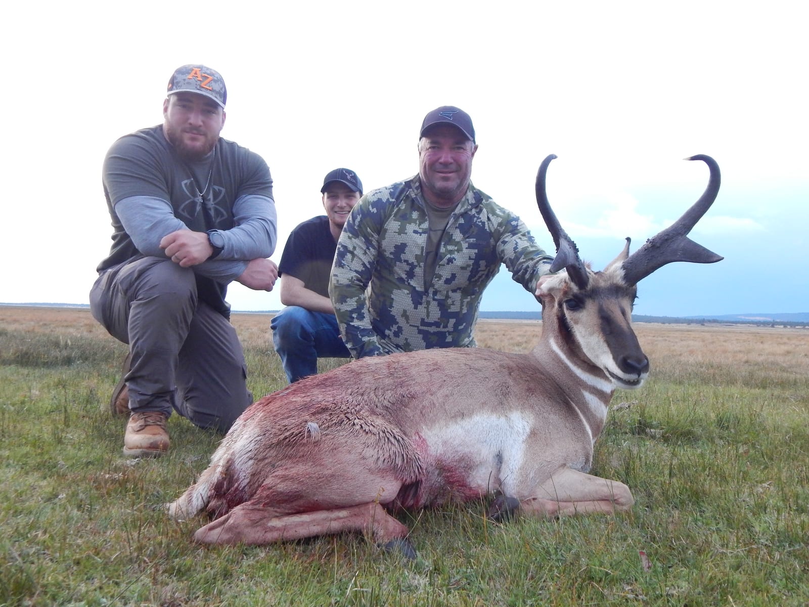 Two hunters pose with a harvested pronghorn in a grassy field.
