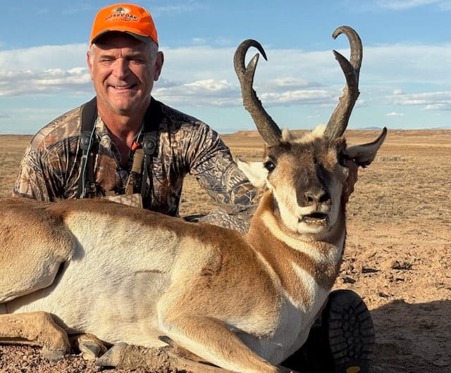 A hunter poses with a harvested pronghorn in a dry, open field.