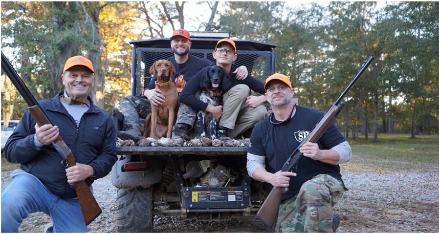 Four hunters and two dogs pose with a harvest of northern bobwhite quail in the back of a utility vehicle.