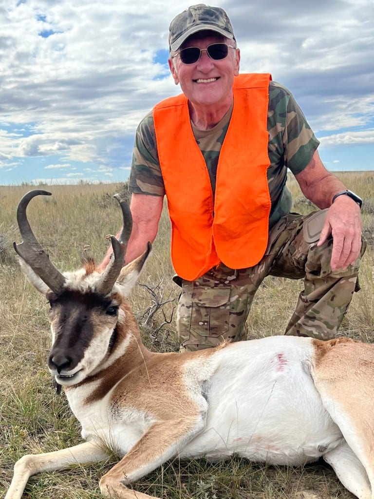 A hunter kneels next to a harvested pronghorn in a grassy field.