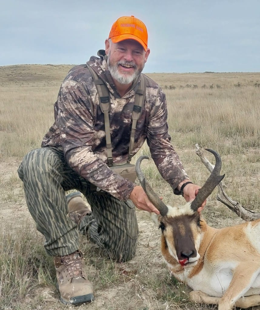 A hunter kneels in a field, posing with a harvested pronghorn.