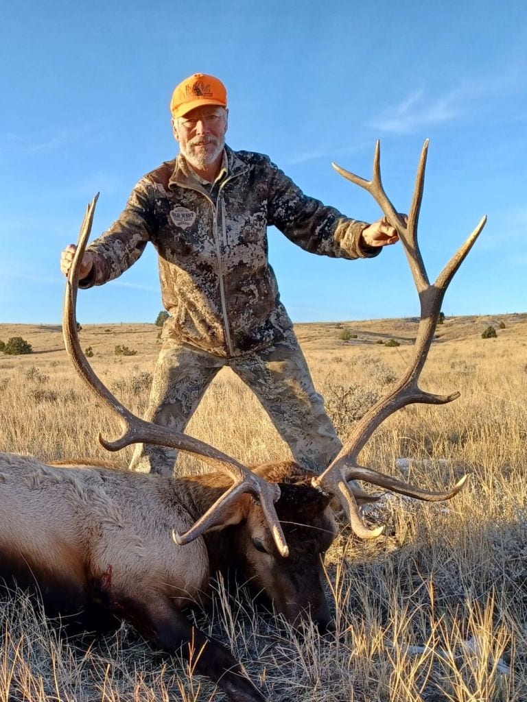 A hunter poses with a harvested elk in a field.