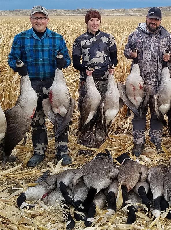 Three hunters pose with their harvested Canada Geese in a field.