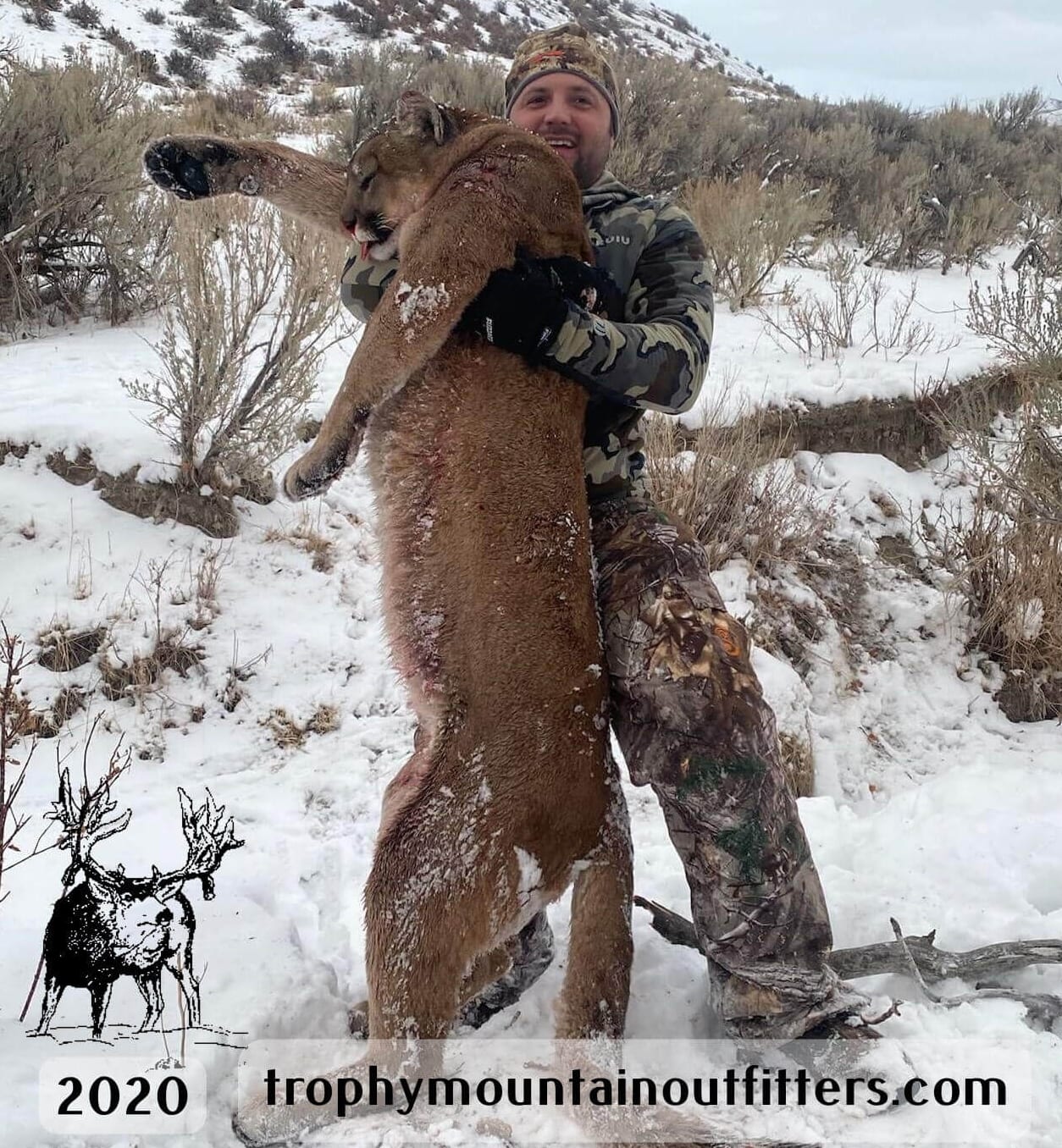 A hunter poses with a harvested mountain lion in a snowy landscape.