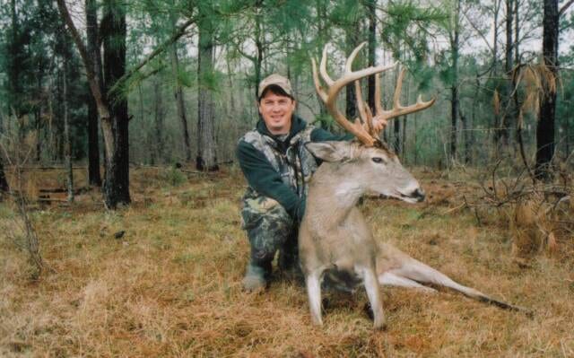 A hunter kneels next to a harvested whitetail deer in a wooded area.