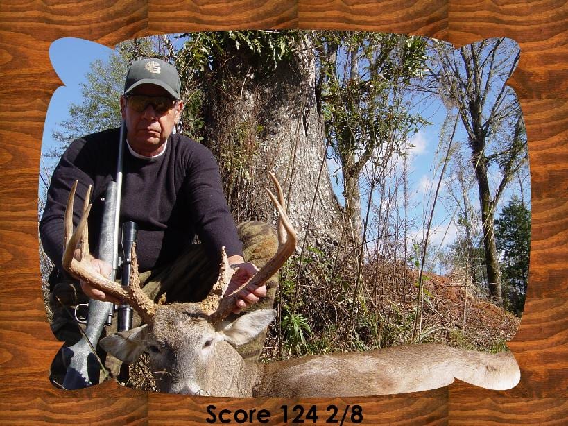 A hunter poses with a harvested whitetail deer in a wooded area.