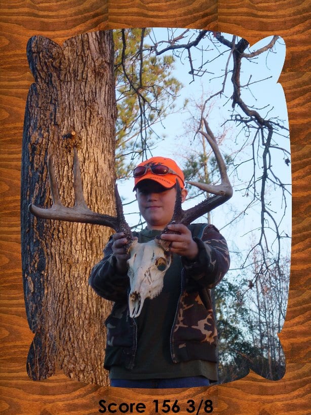 A young person in an orange hat holds a whitetail deer skull with antlers in front of a tree.