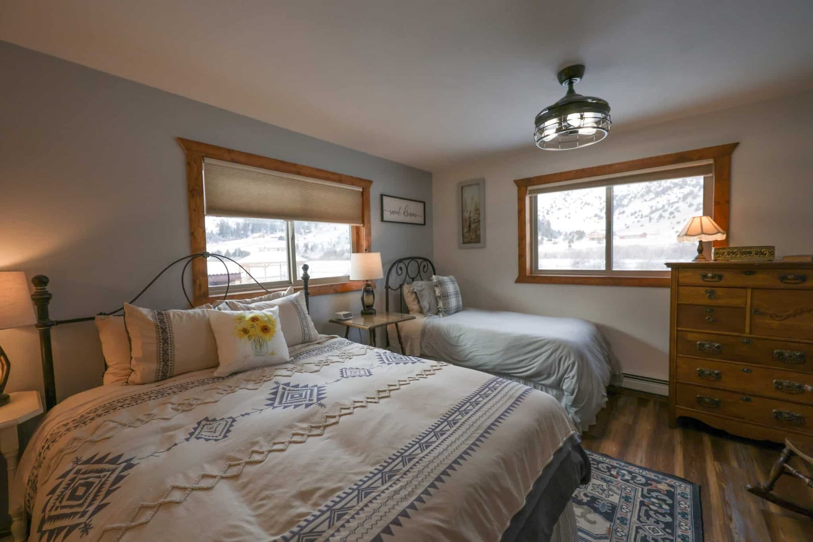 A bedroom with two beds, a dresser, and windows looking out onto a snowy landscape.