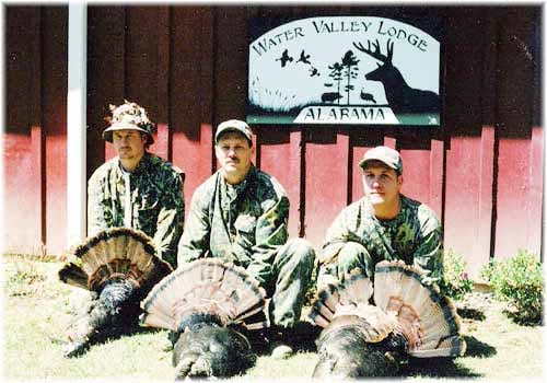 Three hunters pose with three harvested wild turkeys in front of the Water Valley Lodge sign.