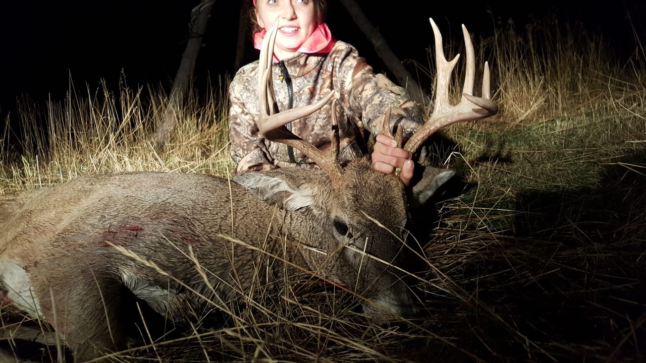 A hunter poses with a harvested whitetail deer at night.