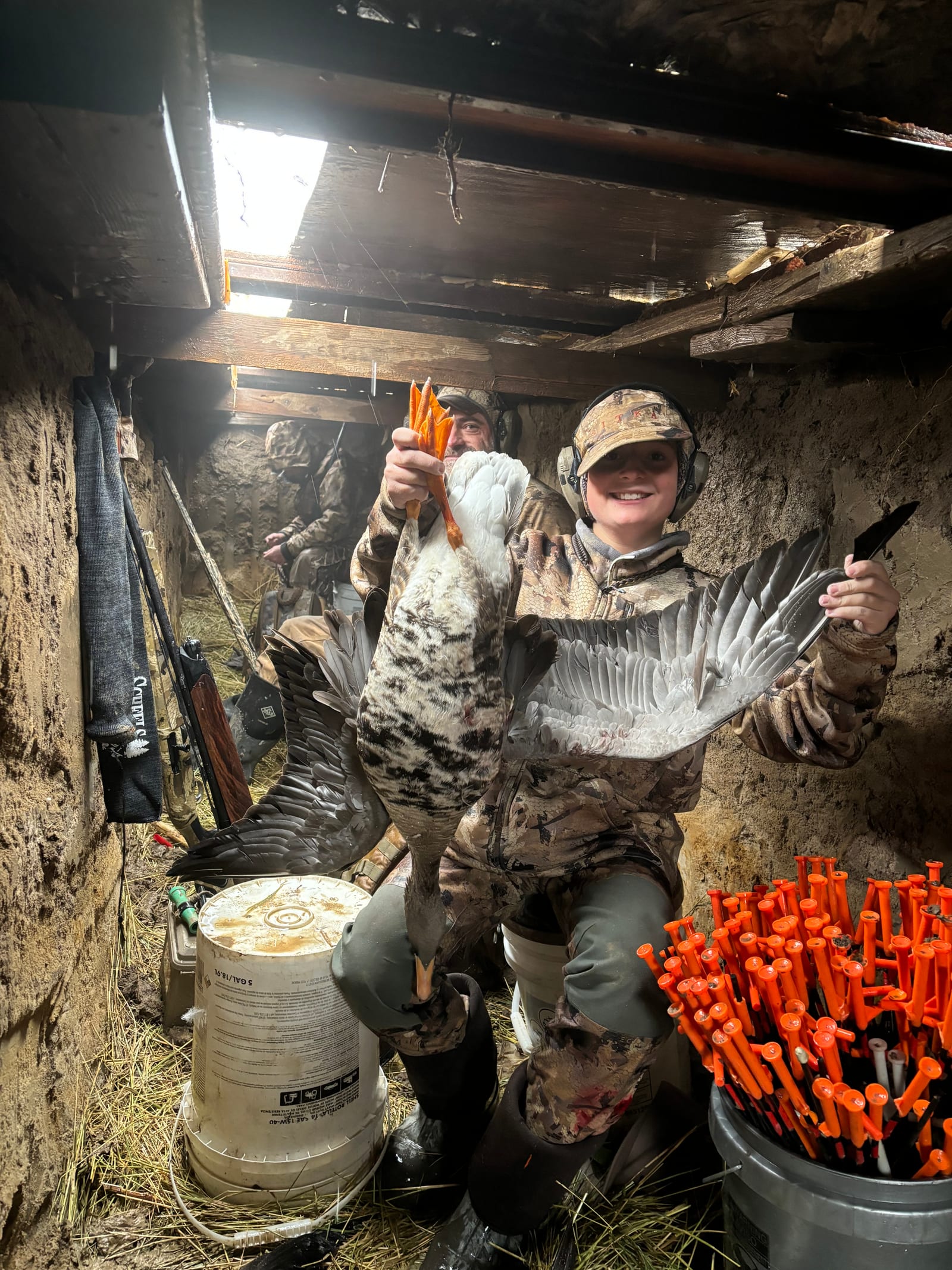 Two hunters pose with harvested snow geese in a duck blind.