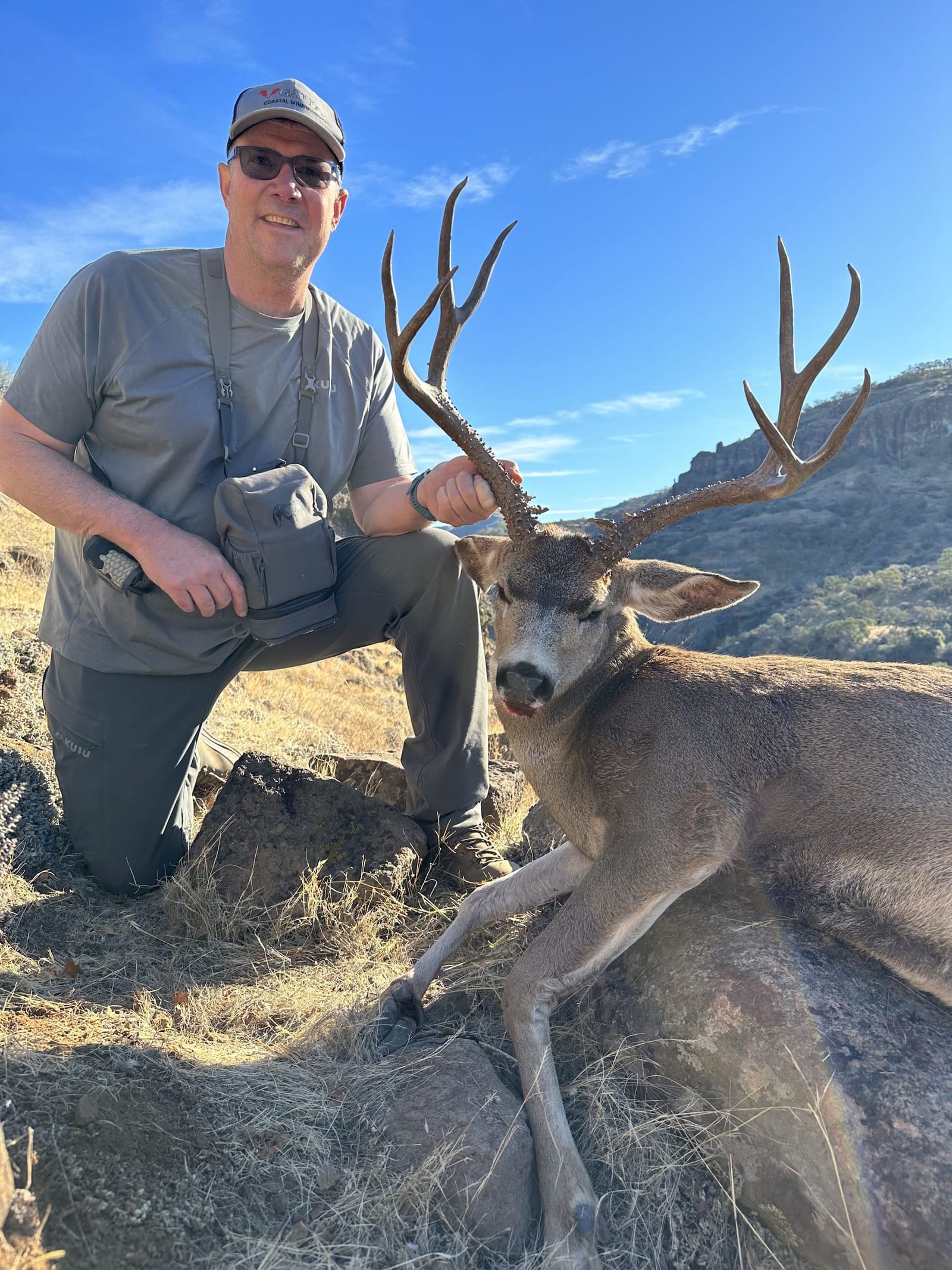 A hunter kneels next to a harvested mule deer.
